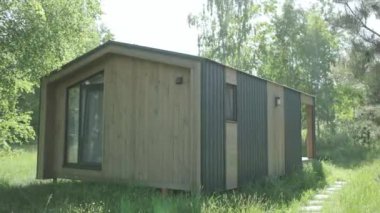 Mütevazı bir bina, Modern Tiny House, çayırın yemyeşil çimlerinin arasında duruyor. Yakınlardaki ağaçlar ve bitkiler resim sahnesine eklenir