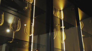 Bir sıra şarap kadehi cam bir rafta mükemmel bir şekilde dizilmiş, görsel olarak hoş bir görüntü yaratıyor. Zarif ve sofistike bir ortam lüks bir hayat tarzı sergilemek için idealdir. 
