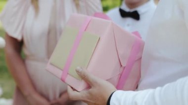 Yakın plan erkek el ele tutuşması hediyesi. Düğün hediyesi, doğum günü hediyesi. Hediye pembe bir kurdeleyle sarılmış pembe bir kağıda sarılmış. Yüksek kaliteli FullHD görüntüler