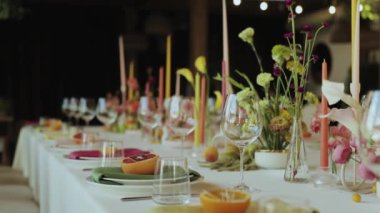 Tabaklar, mumlar ve çiçeklerle süslenmiş güzel bir masa düğünde özel bir etkinlik için büyüleyici bir ortam yaratıyor, ağır çekim, 4k.