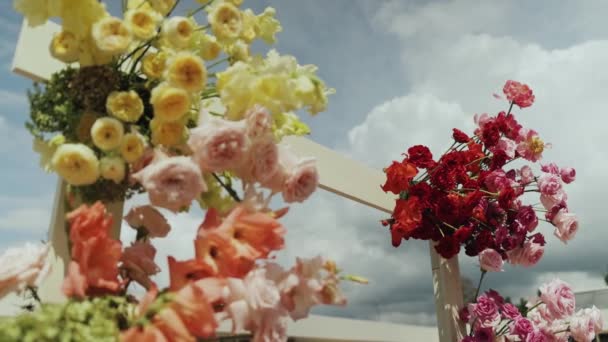 結婚式のアーチを閉じる カラフルな花の花束は 曇った空の背景に設定されたテーブルを飾ります 鮮やかな花びらは上記の灰色の雲と美しく対照しています — ストック動画