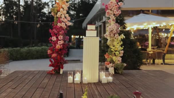 Bröllopstårtan Mot Bakgrund Bröllopsbågen Dekorerad Med Blommor Och Ljus Skapa — Stockvideo