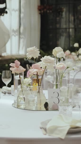 結婚式のテーブルでガラス花瓶にバラのパステル入札ブーケ テーブルの上にガラスの花瓶がたくさん ワイングラスとプレート オレンジ色の結婚式 ゆっくりとした動き 高品質の4K映像 — ストック動画