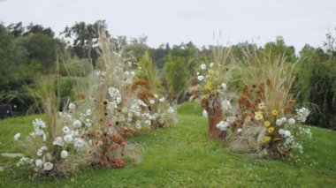 Kurumuş ve yeşil çimenlikte pastel çiçeklerden oluşan etnik boho düğün kemeri, parkta düğün töreni, arka planda yeşil çimenler ve orman, yaz aylarında yavaş çekim. Yüksek kalite 4k görüntü