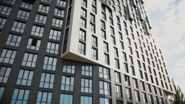 Gökyüzü güneşli bir zemine karşı birden fazla penceresi, balkonları ve modern bir cephesi olan yüksek katlı bir apartman dairesini gözler önüne seren kentsel bir tasarımın videosu.