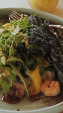 Masada çatalla servis edilen tabakta sunulan yeşil sebzeler de dahil olmak üzere taze malzemelerle hazırlanmış lezzetli bir yemek. Dikey video