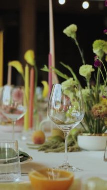 Tabaklar, mumlar ve çiçeklerle süslenmiş güzel bir masa düğünde özel bir etkinlik için büyüleyici bir ortam yaratıyor, ağır çekim, 4K. Dikey video