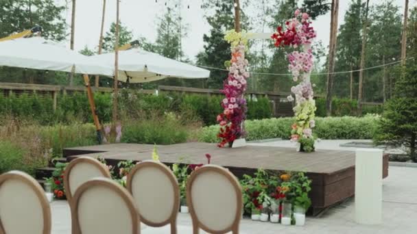 花と椅子に囲まれた魅力的な木製ステージが結婚式を待っています 椅子のローズは正面にきちんと配置され ロマンチックでエレガントな雰囲気を作り出しています ウェディングアーチ — ストック動画