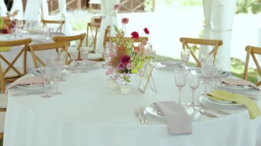 Zarifçe masa takımları, çiçekler ve çiçeklerle dolu masaları bir düğün resepsiyonu için çadırın altına kurun. Sandalyeler, mobilyalar ve içecek takımı çarpıcı iç tasarımı tamamladı