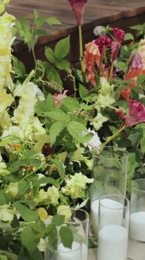 Çiçekli ve mumlu vazolardan oluşan bir sıra, düğün kemerinin yanındaki kaldırımı süslerken, parlak renkler ve mis kokulu aromalı binaların manzarasını aydınlatıyor. Dikey video