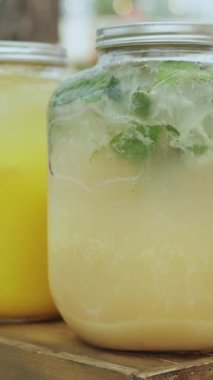 Limon suyu, limon suyu ve kokteyl gibi çeşitli sıvı içecekler içeren kavanozlar ahşap bir masada sergilenir. Yakın plan. Dikey video