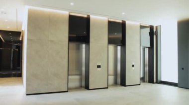 Bir binanın içinde bir sıra asansör düzenlenir, her bir kabin, kapı kolları ve gaz armatürleri olan dikdörtgen bir kabin içerir.