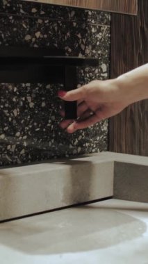Bir kadının eli banyoda siyah bir musluğu çevirir. Su akıyor. Karanlık banyo, siyah musluk ve mermer lavabo, yavaş çekim. Yüksek kalite 4K görüntü. Dikey video