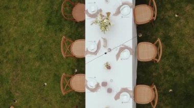 Bir festival masası ve dışarıda yeşil bir çimenlikte bulunan ahşap sandalyelerin havadan görüntüsü. Düğünün en üst masalarından yakın çekim görüntüsü. Düğün... 4 bin dolarlık kaliteli bir çekim. Dikey video.
