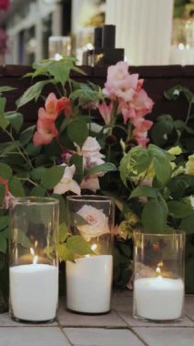 Düğünden önce bir grup mum bir düğünde yerde duruyor. Pembe yapraklar güzel bir çiçek aranjmanı oluşturuyor. Dikey video