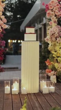 Düğün pastası, düğün kemerinin arka planında çiçek ve mumlarla süslenerek büyülü bir atmosfer yaratılıyor ve odaya biraz doğa katıyor. Dikey video