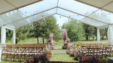 A beautifully arranged outdoor wedding with aligned chairs, vibrant flowers, and a lovely tented canopy