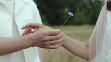 Hassas bir çiçeği nazikçe değiş tokuş eden bir çift, doğada romantik ve samimi bir anı güzel bir şekilde yakalıyor.