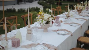 Güzel çiçekler, titreyen mumlar ve kırsal sandalyelerle süslenmiş sofistike ve zarif bir açık hava yemek düzeni.