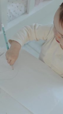 Genç bir çocuk, yaratıcılığını ve erken öğrenme yeteneklerini gösteren büyük beyaz bir çarşafa neşeyle resim çizer.