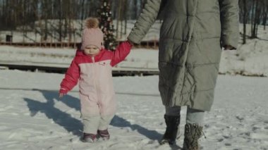 Karlı zeminde yürüyen bir ebeveyn ve çocuğun, sıcaklığı ve bağlantıyı yakaladığı neşeli bir kış sahnesi..