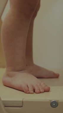 Eski ahşap bir basamakta duran çıplak, küçük ayaklı bir çocuğun yakından görüntüsü masumiyeti gösteriyor ve artan bir merak.