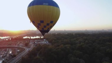 Güzel bir sıcak hava balonu gün doğumunda yemyeşil çimlerin üzerinde süzülür. Zamandaki huzurlu bir anı yakalar.