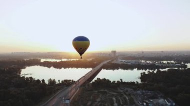 Canlı ve renkli bir sıcak hava balonu berrak gökyüzünde süzülüyor sakin bir su manzarasının üzerinde güzel bir gündoğumunda.