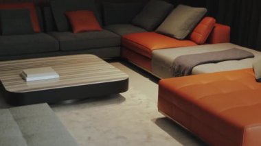 Çağdaş oturma odasında, ahşap sehpası olan turuncu ve gri renkli parlak bir kanepe var..