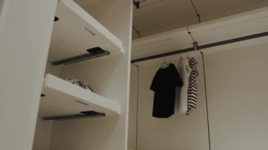 Basit giysi seçeneklerinin yanı sıra organizasyon için geniş raf alanı içeren gösterişli ve minimalist bir dolap tasarımı.