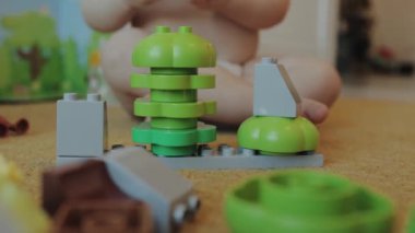 Genç bir çocuk yere yayılmış canlı yeşil lego bloklarıyla neşe içinde oynuyor, yaratıcı oyunlarla meşgul.