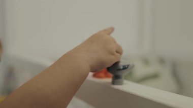 Bir çocuk renkli bir oyuncağa uzanır, meraklarını ve gelişim duygusunu vurgular.