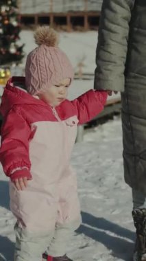 Kış kıyafetleri içinde mutlu bir çocuk karda oynar, bir yetişkinin elini tutar, neşeli, büyülü bir sahnede. Dikey video