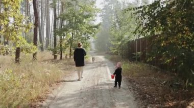 Neşeli bir yetişkin ve heyecanlı bir çocuk neşeli bir sonbahar ormanında sevgili köpekleri eşliğinde geziniyor.