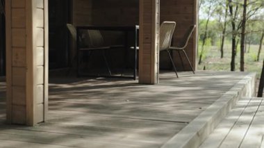 Sakin bir açık hava manzarası ahşap bir güverte, rahat sandalyeler ve bol miktarda doğal yeşillik ile sergilenir.