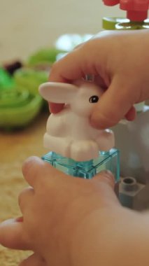 Dikey video. Bir çocuk neşeli bir şekilde beyaz bir tavşan oyuncağını renkli bir bloğa yerleştirir, yaratıcılığı ve yaratıcı oyunu teşvik eder.