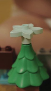 Dikey bir video bir çocuk küçük bir el dikkatle dekore ediyor canlı yeşil LEGO Noel ağacı üzerinde neşeli bir yıldız ile