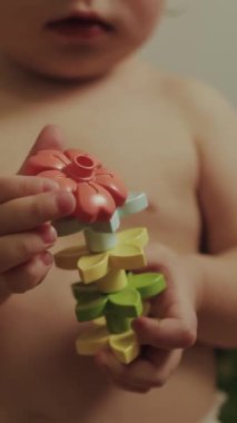 Dikey video. neşeli bir çocuk renkli çiçeklerle dolu oyuncakları istifliyor, yaratıcılıklarını ve hayal güçlerini sergiliyor.