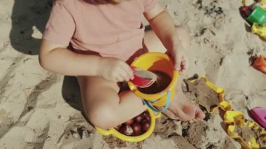 Neşeli ve tasasız bir çocuk kumla ve renkli plaj oyuncaklarıyla oynayarak güneşli güzel bir günün tadını çıkarıyor.