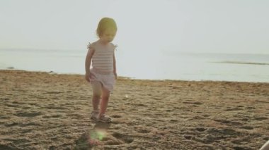 Küçük bir çocuk, sakin denizin yanında çocukluğun saf mutluluğunu yakalayan kumlu kumsalda neşeyle gezer.