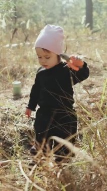 Neşeli bir çocuk, açık havada, sıcacık, siyah bir kıyafet içinde, doğayı kucaklayarak neşeyle keşfeder. Dikey video. 