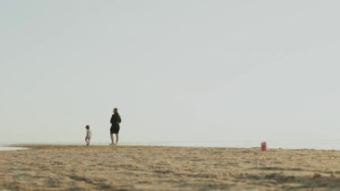 Harika sakin bir sahil sahnesi sevgi dolu bir ebeveyni ve neşeli çocuklarını sahile doğru sessiz bir yürüyüşe çıkarıyor.