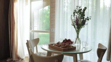 Parlak bir yemek alanında canlı çiçeklerle ve cazip hamur işleriyle atmosferi geliştiren şık cam bir masa vardır.