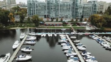 Huzurlu ve huzurlu bir marina sahnesinde modern, çağdaş binaların yanında lüks tekneler sergileniyor.