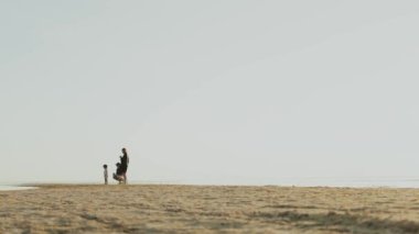 Sevgi dolu bir anne ve babanın ve çocuğun kumsalda birlikte vakit geçirdiği, sevgiyi ve doğayı somutlaştırdığı sakin bir sahne.