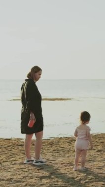 Dikey video. Sahilde bir anne ve çocuğu arasındaki hassas bir an ailenin ve huzurun özünü yakalıyor..