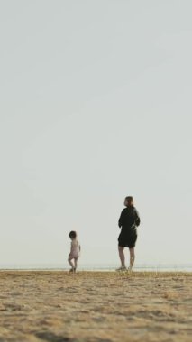 Dikey video. Huzurlu bir ortamda, bir anne ve çocuğu kumsalda sakin ve huzurlu bir gezintinin tadını çıkarırlar.