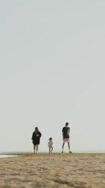 Huzurlu bir sahilde neşeyle yürüyen bir aile, beraberliğin ve huzurun güzel bir anını yakalar.