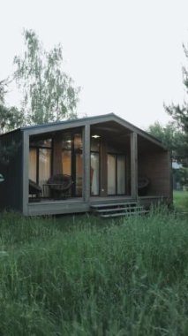 Dikey video. Güzelce tasarlanmış çağdaş bir ev, doğa meraklıları için ideal, uzun otlar ve gür ağaçların arasında yuva yapar.