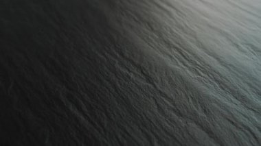 Sakin, karanlık bir su yüzeyinin yumuşak ve nazik dalga desenleri içeren soyut bir tasviri.